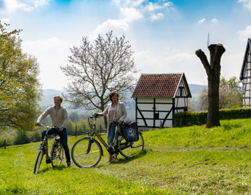Twee fietsers staan in een weiland met vakwerkhuisjes