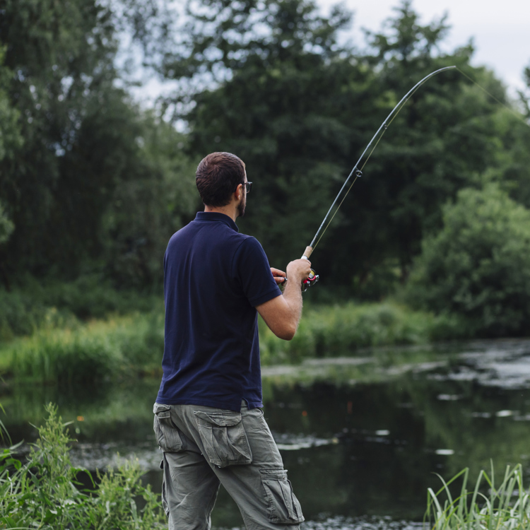 Man met blauwe polo hangt zijn vishengel in een visvijver omringd door een groenrijke omgeving. 