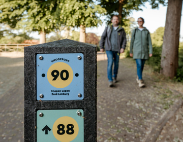 Knooppuntenpaaltje met twee wandelende mensen in de achtergrond